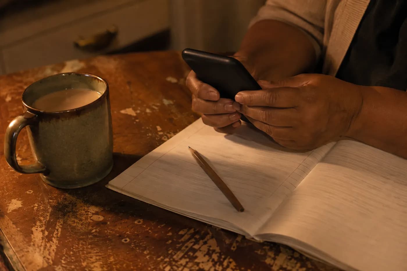 An adult holding a phone above an open exercise book on a kitchen table